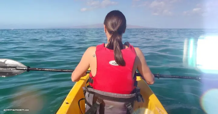 Kayaker in a yellow kayak paddling on calm blue water off Mākena