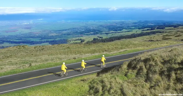 Cyclists in yellow jackets riding down a Haleakalā road with Upcountry Maui views below