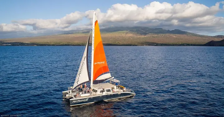 Catamaran with an orange sail cruising off Mākena in South Maui