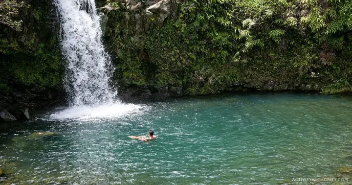 Swimmer in a jungle pool below a waterfall on the Halfway to Hana tour