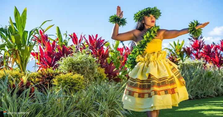 Hula dancer in a yellow dress and leaf lei among tropical gardens at the Royal Lahaina Luau in West Maui