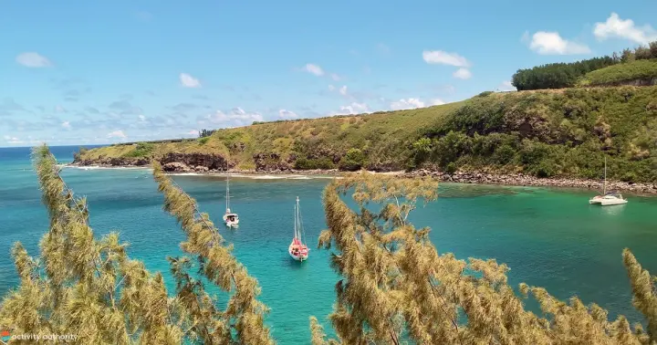 Sailboats anchored in a calm turquoise bay below green cliffs in West Maui